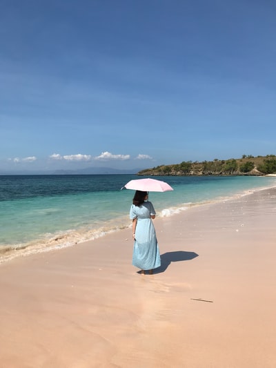 女人在白色礼服粉色雨伞走在海滩白天
